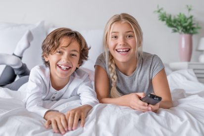 Happy childrens in pajamas lying in bedroom at home watching tv